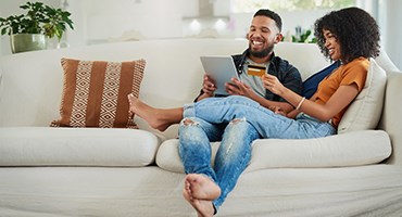 Couple sitting on couch in living room shopping for insurance online, laptop